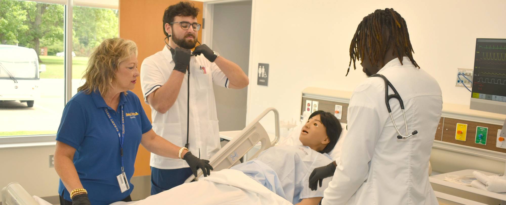 Two health science students working with a simulation manikin under the guidance of an instructor.