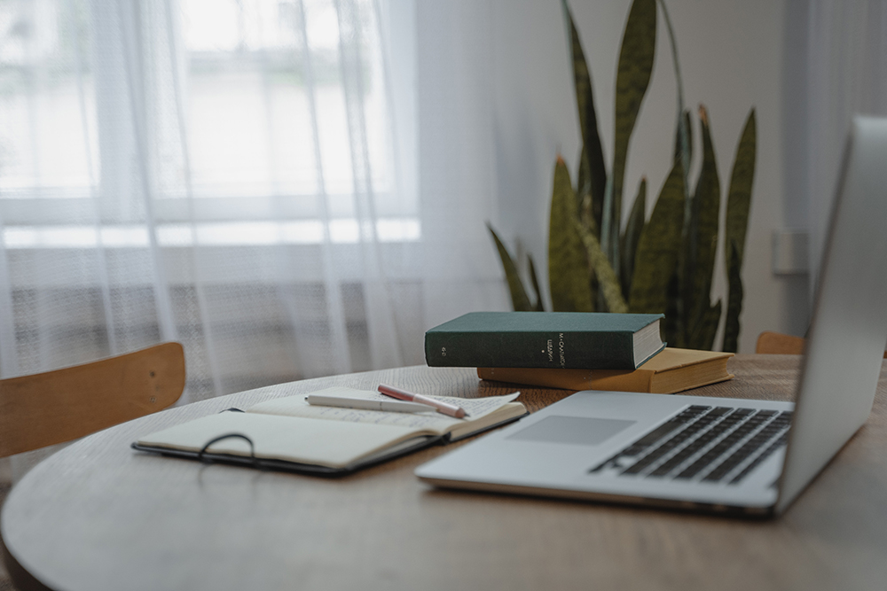 Laptop with books and an open notebook with pens resting on top